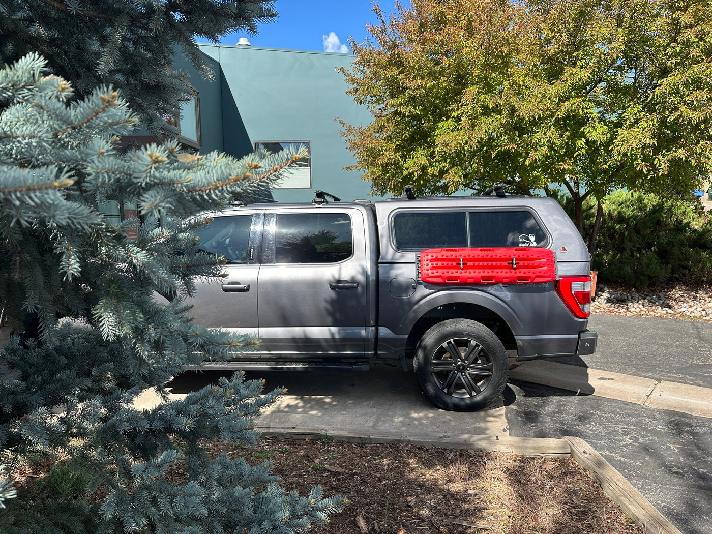 2025 Ford F150 with a Leer fiberglass capper and STAPLL 48x10 Fender Racks, the capper's exterior lip notched for the brackets